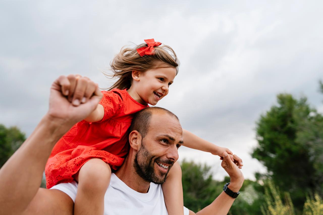 Happy Man carrying cheerful daughter on shoulders