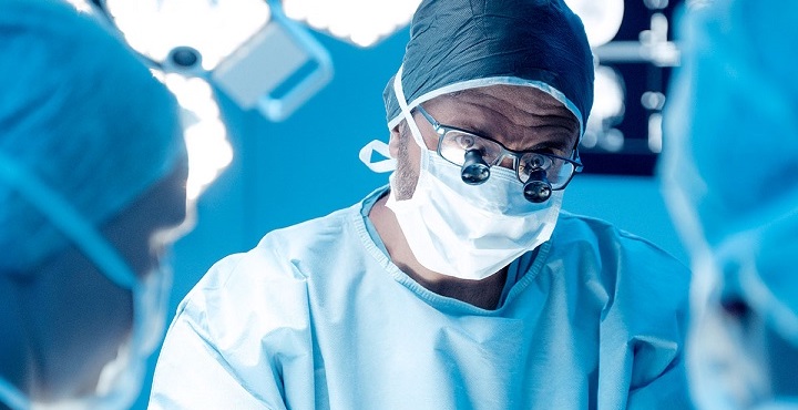 male surgeon in operating room under bright lights and with magnifiers on his glasses